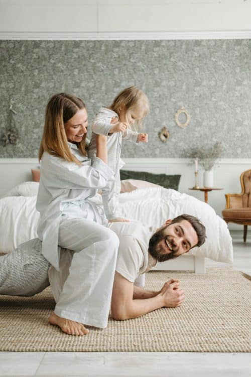 A young family wrestles on the ground of a bedroom
