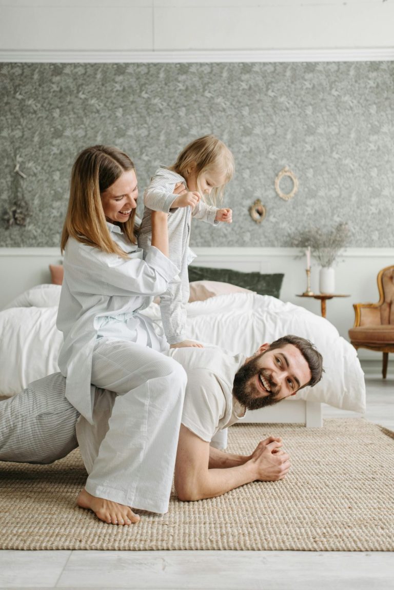 A young family wrestles on the ground of a bedroom