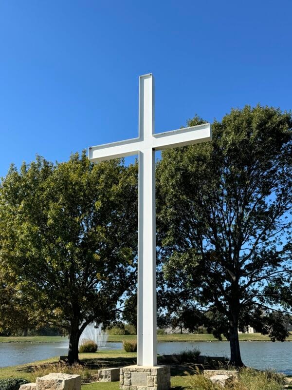 picture of a cross in front of trees and a pond